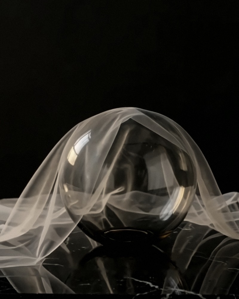 A glass sphere under a sheer veil on black marble